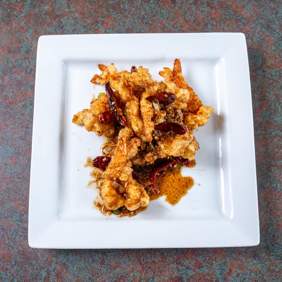 Ming's Restaurant's crispy fried shrimp with chili peppers and sauce on a white plate.