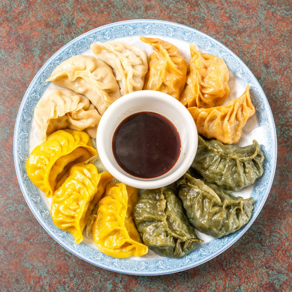A blue and white plate of colorful Ming's Restaurant dumplings with a small bowl of dipping sauce.