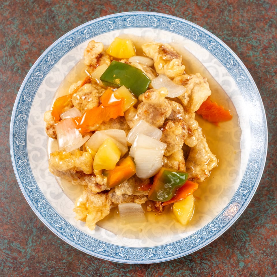 Sweet and sour chicken with pineapple, bell peppers, and onions on a blue and white plate.
