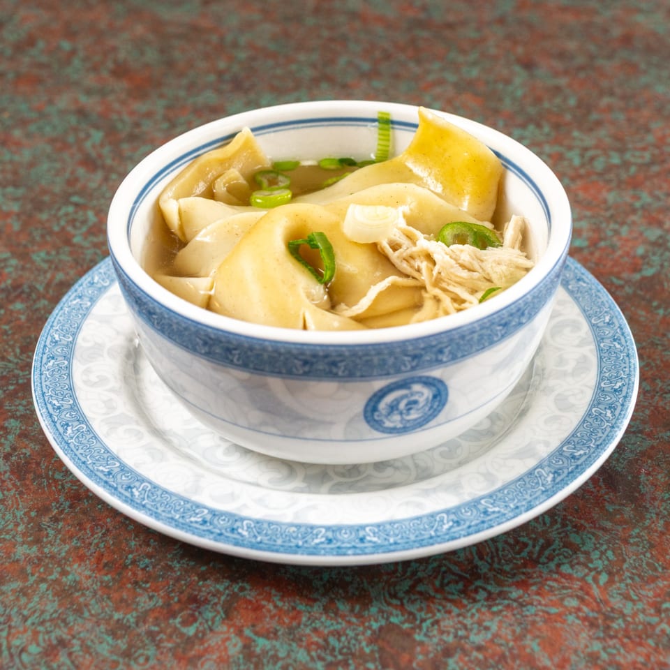 A bowl of wonton soup with shredded chicken and green onions on a patterned plate.
